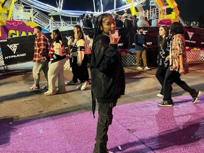 Jirah Mayweather is showing rock sign as there is Ferris wheel in the background.